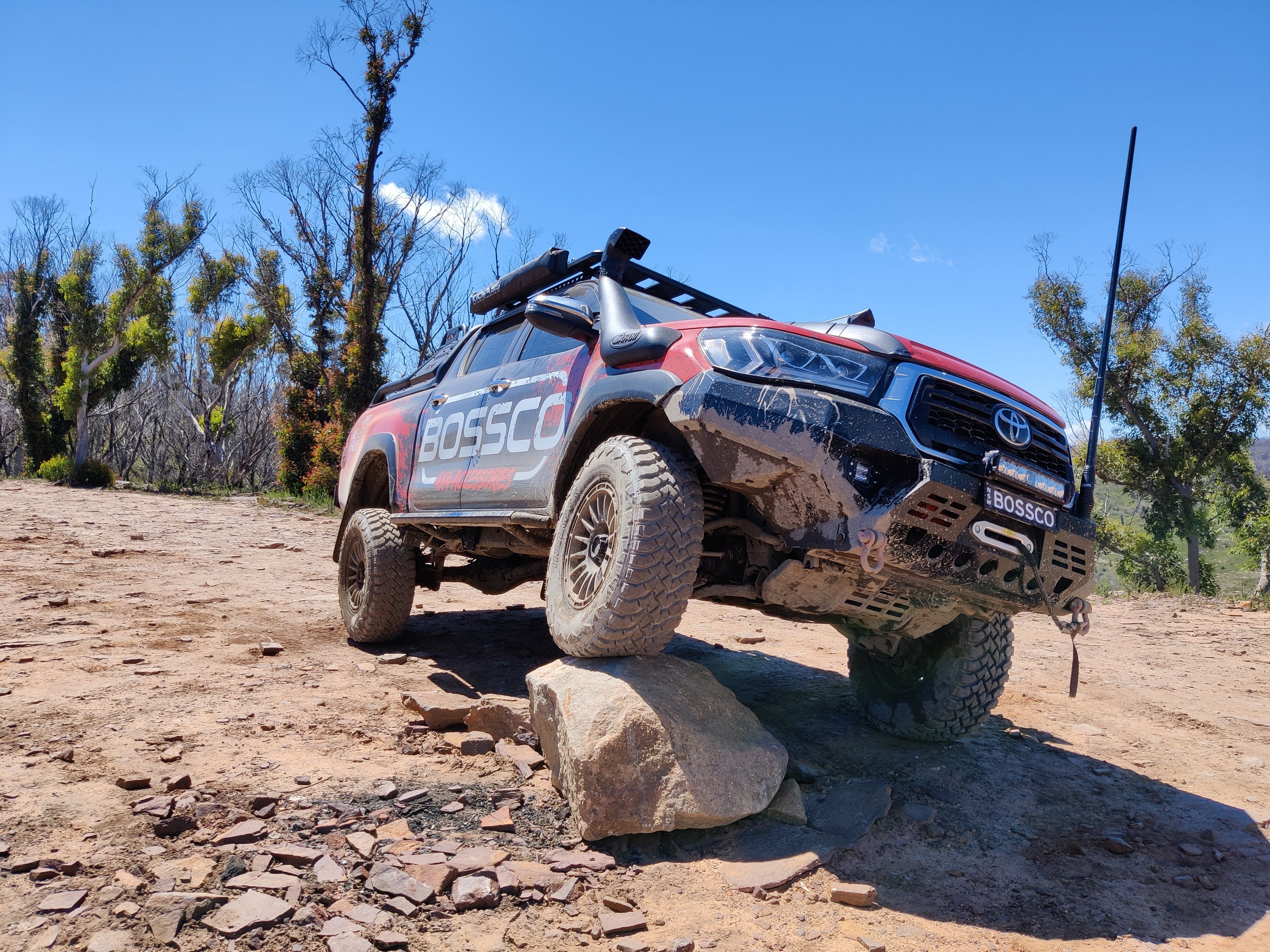Bossco 4x4 Accessories red pickup truck off-roading with a bullbar, roof rack bars, bull bar suitable antenna and 4WD recovery gear